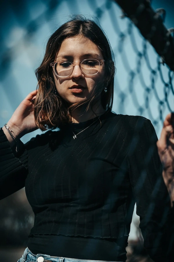 Femme portant des lunettes et un haut noir devant une clôture en maillon de chaîne